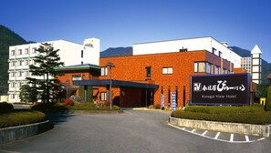 Situated amidst mountains, the Kasugai View Hotel features a modern design with brick and white exterior walls, set amidst well-maintained landscaping.