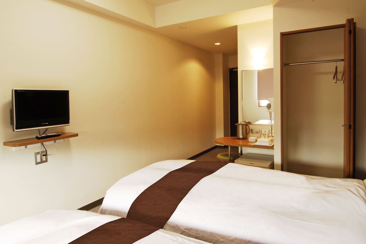 A hotel room with two beds, a television, a desk with a lamp, and a wardrobe.