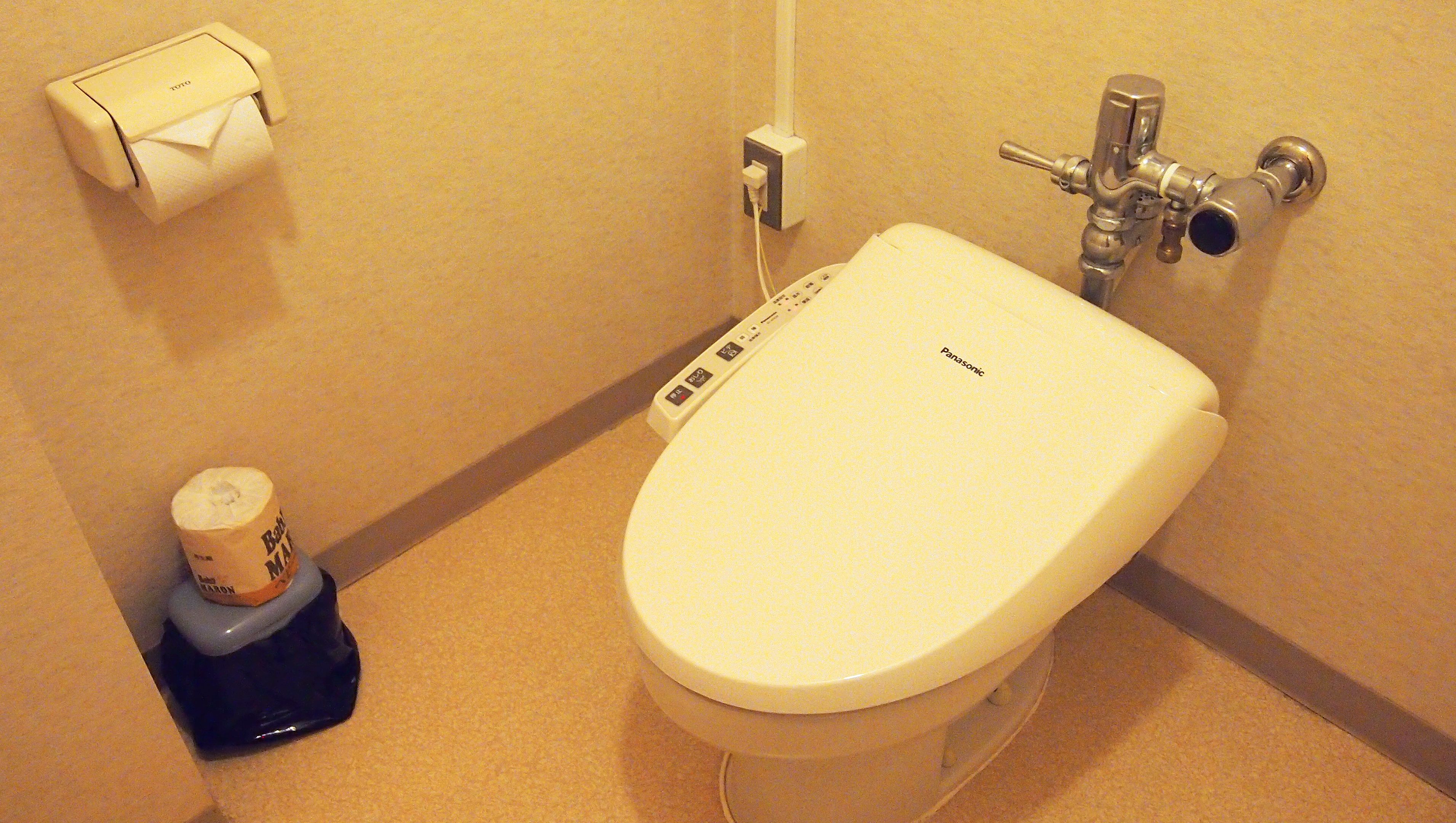 A bathroom with a toilet, a paper towel dispenser, and a bidet.