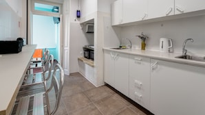 A modern kitchen with white cabinets, a stainless steel sink, and a dining area with metal chairs. - Hostel Seven Hills (Lisbon)