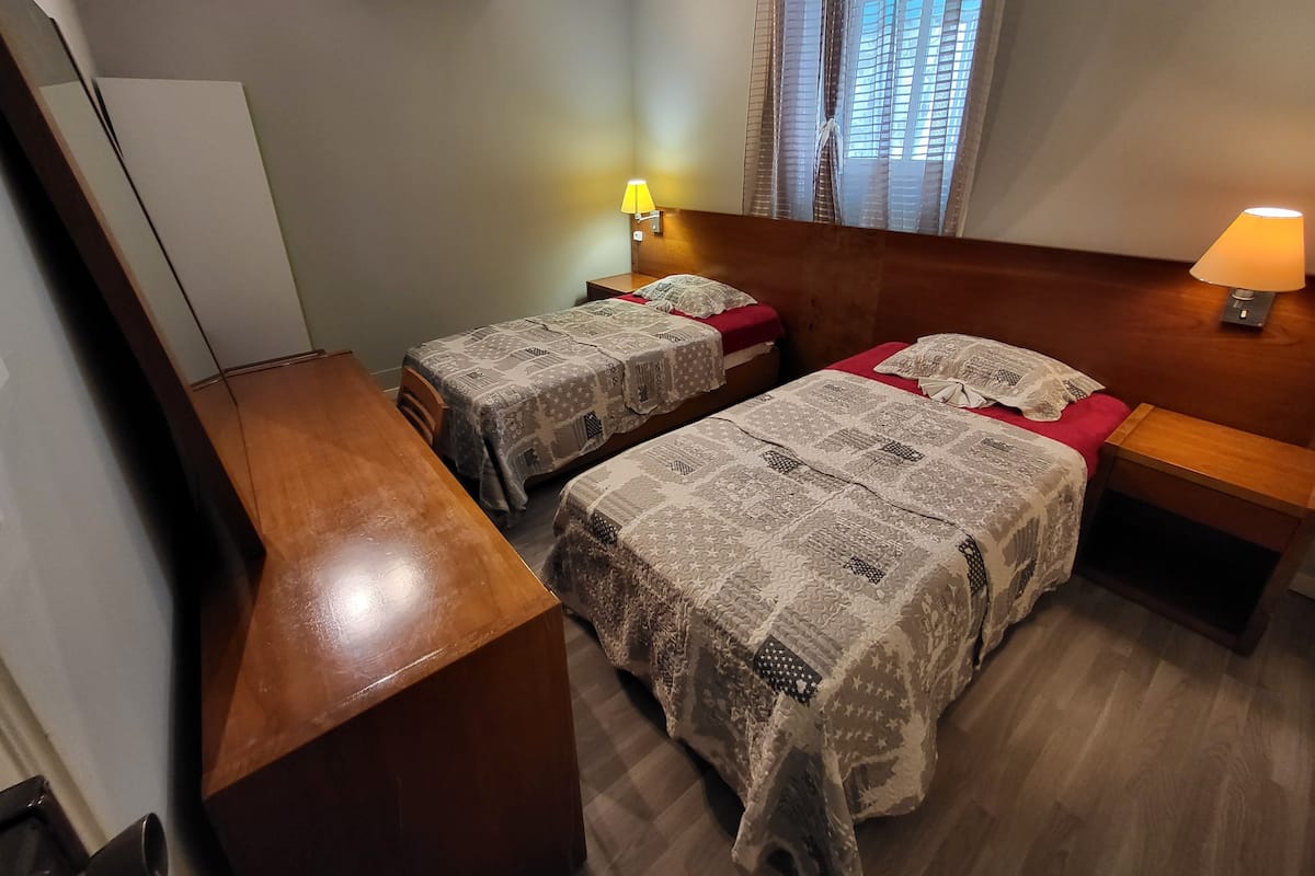 Ein Hotelzimmer mit zwei Betten, Holz-Kopfteilen, einem Schreibtisch und einem Nachttisch mit Lampen.