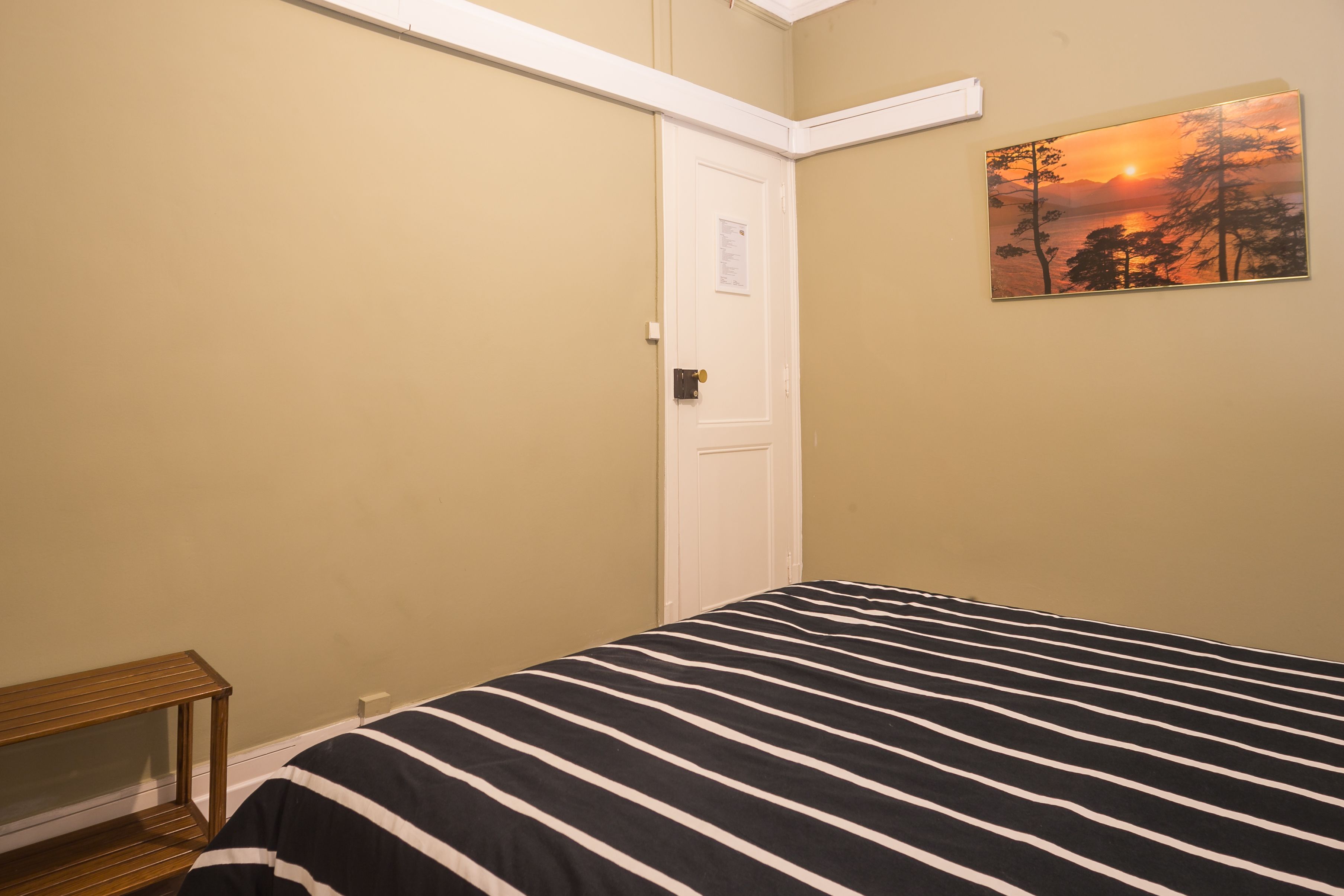 Un dormitorio con una cama, una puerta y un cuadro en la pared.