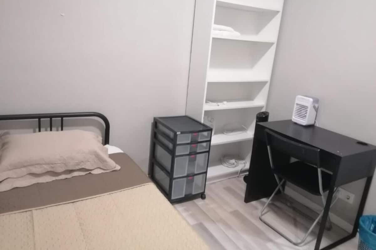 Ein Schlafzimmer mit Bett, Schreibtisch, Regale und einem kleinen Rollwagen.
