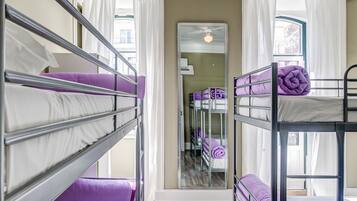Una habitación con literas, cortinas blancas y un ventilador de techo.