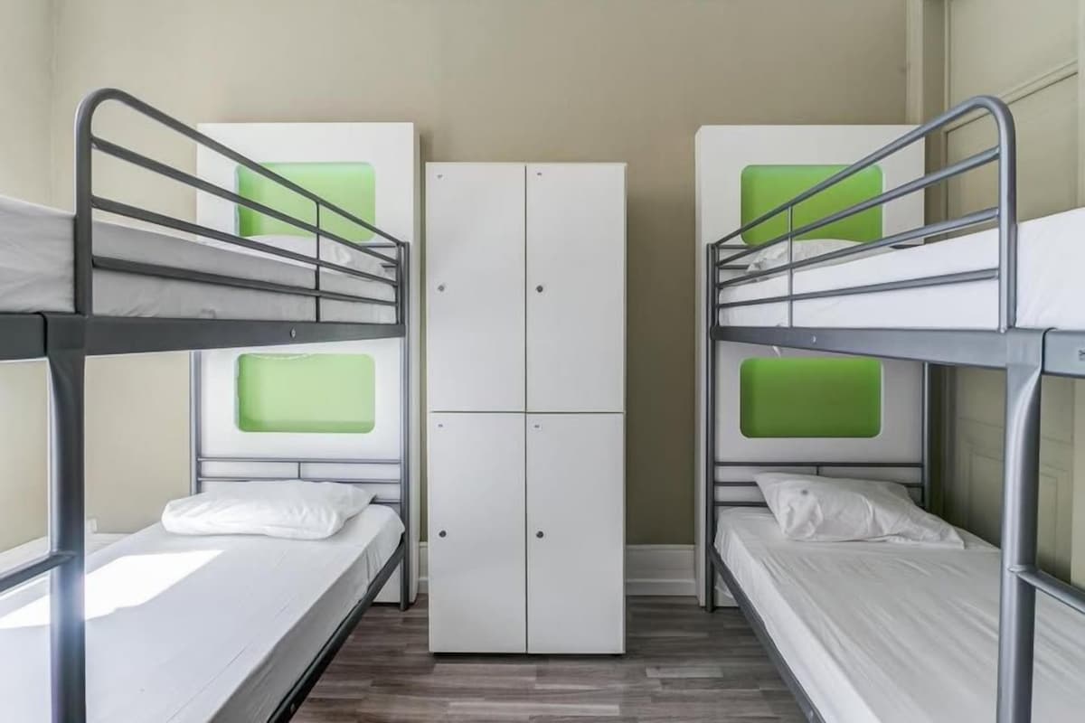 A dormitory room with bunk beds, a wardrobe, and a window.