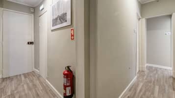 Um corredor com um extintor fixado na parede, uma porta e um quadro emoldurado.