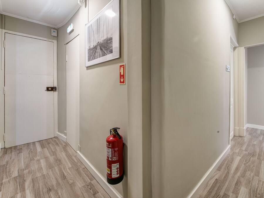 Um corredor com um extintor fixado na parede, uma porta e um quadro emoldurado.