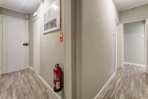 A hallway with a fire extinguisher mounted on the wall, a door, and a framed picture. - Hostel Seven Hills (Lisbon)