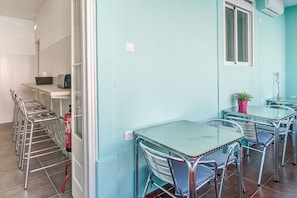 A room with teal walls, metal-framed tables and chairs, a small kitchenette, and a window with blinds. - Hostel Seven Hills (Lisbon)
