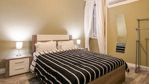 A bedroom with a wooden bed, bedside tables, a mirror, and a window with curtains. - Hostel Seven Hills (Lisbon)