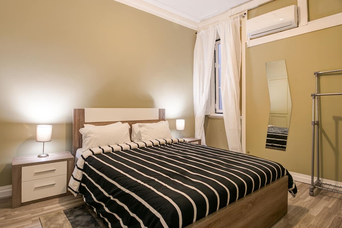 Ein Schlafzimmer mit einem hölzernen Bett, Nachttischen, einem Spiegel und einem Fenster mit Vorhängen.