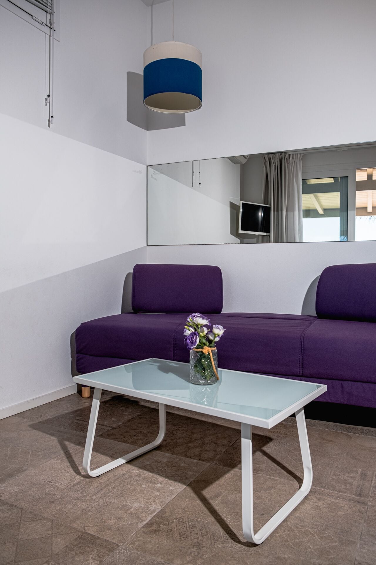 A modern room with a purple sofa, a glass coffee table with a vase of flowers, and a hanging lamp.