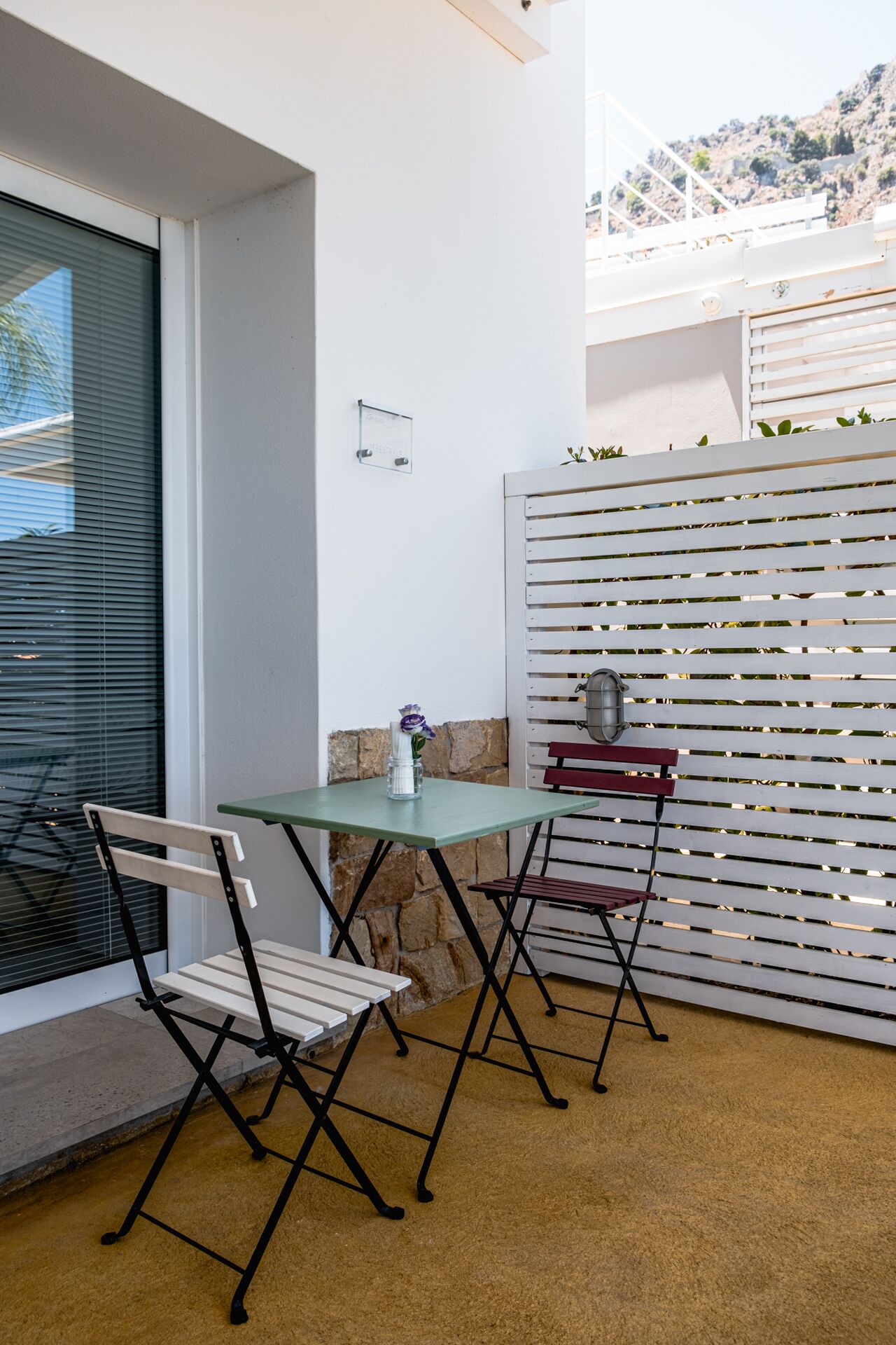 A patio area with a table and two chairs, a stone wall, and a white fence with horizontal slats.