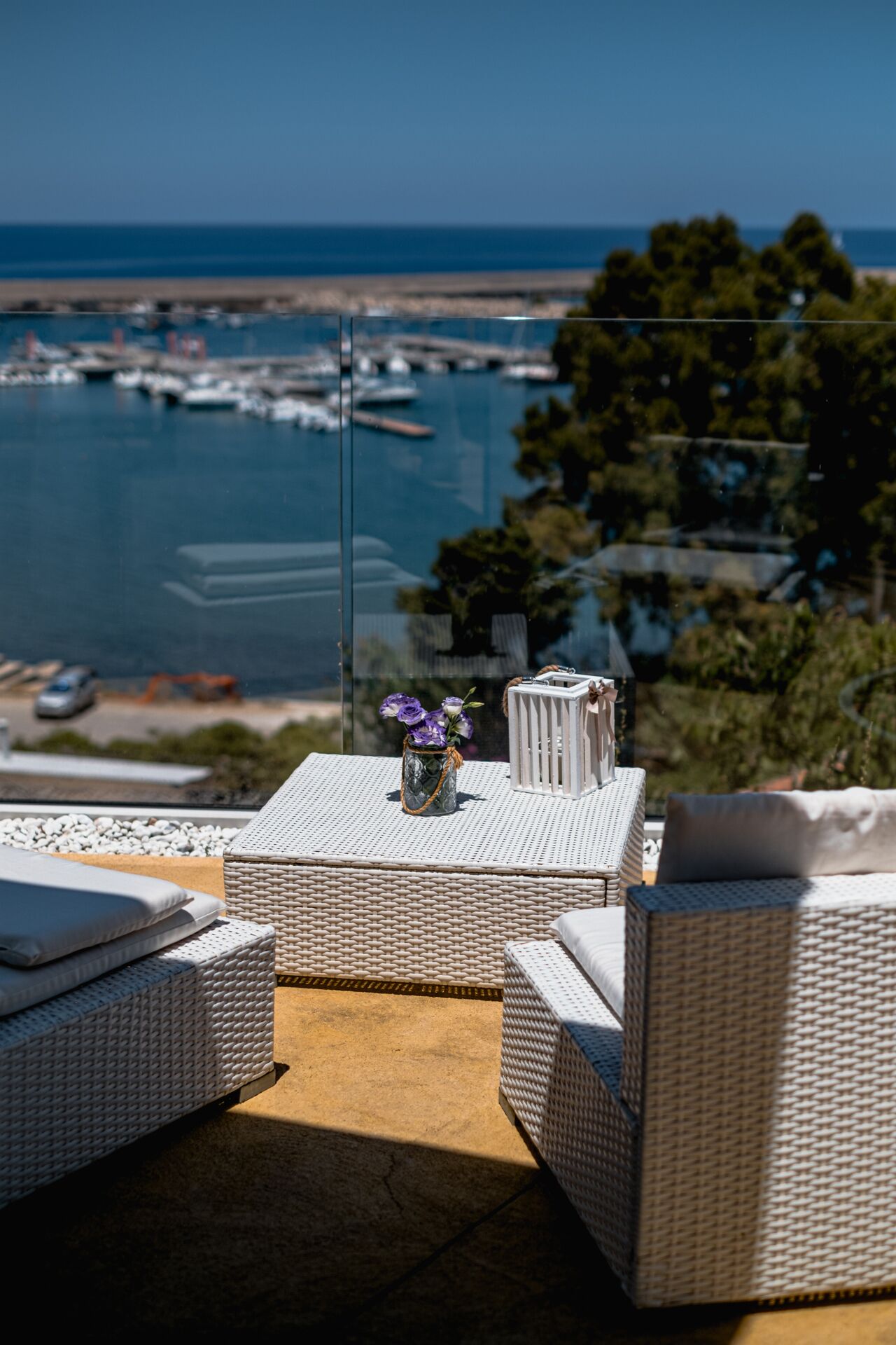A balcony with wicker furniture, a vase with flowers, and a view of the sea and marina.