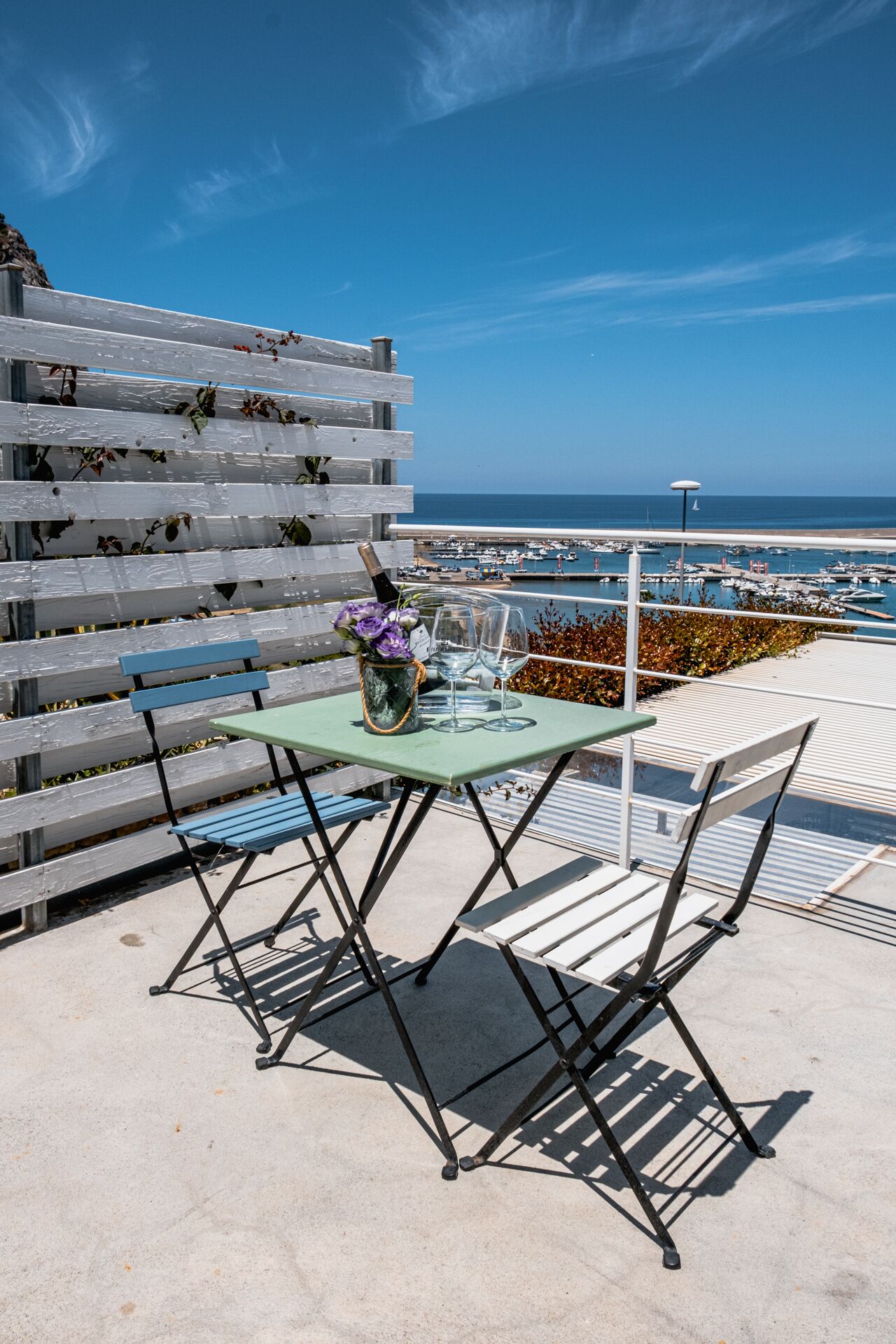 A patio with a table and chairs, a bottle of champagne, and a vase of flowers.