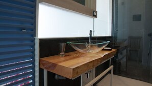A modern bathroom with a wooden vanity, a glass bowl sink, and a glass of water. - A Tonnara (Cefalù)