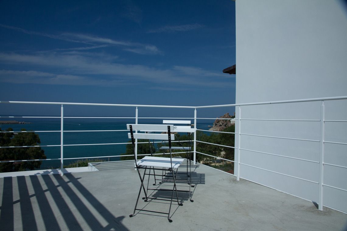 A balcony with a view of the sea, a white railing, and a metal folding chair.