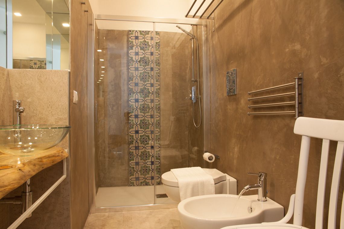 A modern bathroom with a glass shower enclosure, a glass sink, and two toilets.