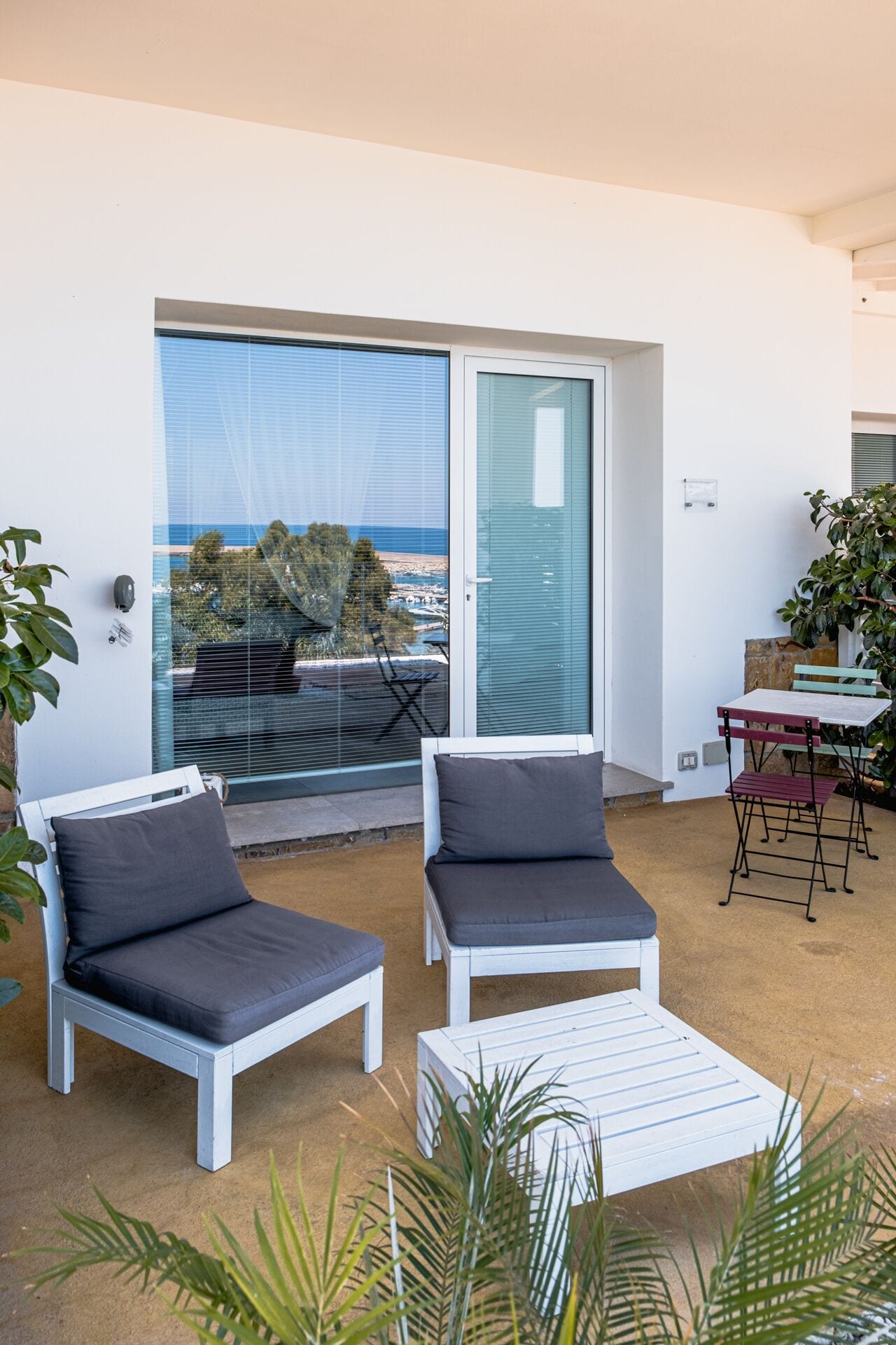 A balcony with two white lounge chairs, a small table, and a potted plant.