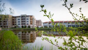 A view of a building complex with multiple floors and a reflective water body in the foreground. - Lighthouse Apartments & Villas (Balchik)