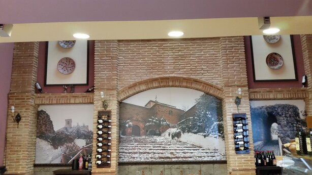 A lobby with a brick wall, a large mural of a snowy scene, and a wine rack with bottles. - Hotel Restaurante Casa Marchena (Vilches)