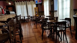 A restaurant interior with wooden tables and chairs, a tiled floor, and a counter with a menu board. - Hotel Restaurante Casa Marchena (Vilches)