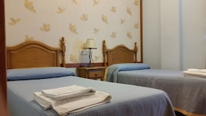 A hotel room with two beds, a nightstand with a lamp, and a wall with a leaf pattern. - Hotel Restaurante Casa Marchena (Vilches)