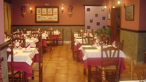 A restaurant with multiple tables and chairs, each set with white tablecloths and red napkins. - Hotel Restaurante Casa Marchena (Vilches)