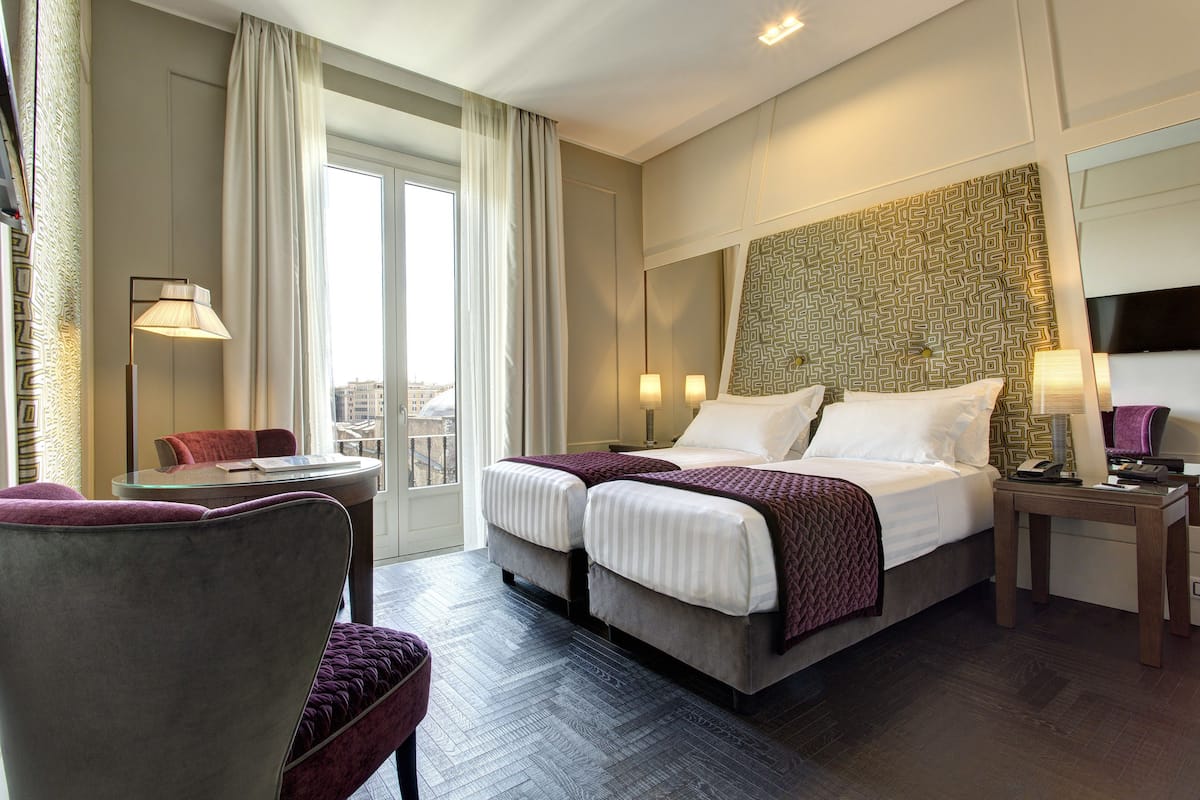 A hotel room with a large bed, two bedside tables, a chair, and a view of the city through the window.