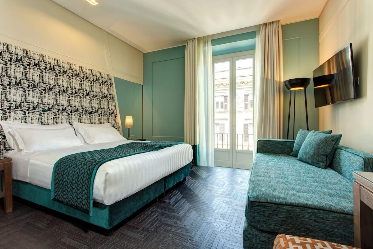 A hotel room with a large bed, a sofa, a TV, and a patterned wall.