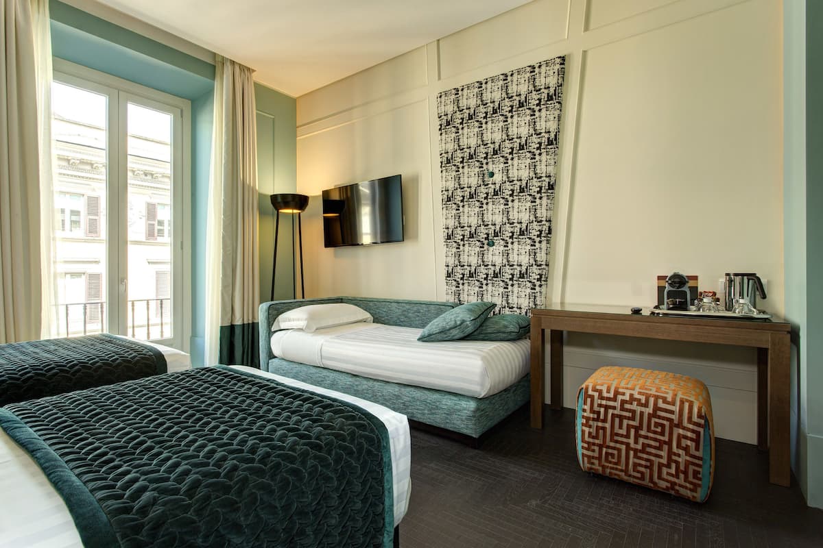 A hotel room with two beds, a desk, a TV, and a patterned wall.