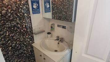 A bathroom with a white sink, a mirror, and a wall covered in pebbles. There are signs reminding to wash hands and stop the spread of germs.