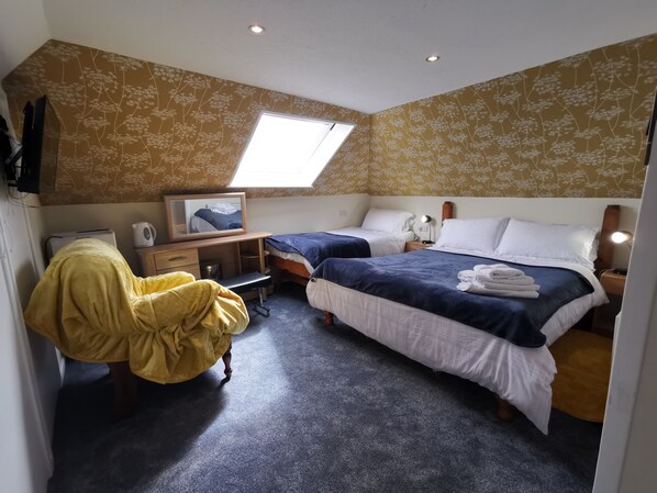 Une chambre avec deux lits, un bureau, une chaise, un miroir et une fenêtre de toit.
