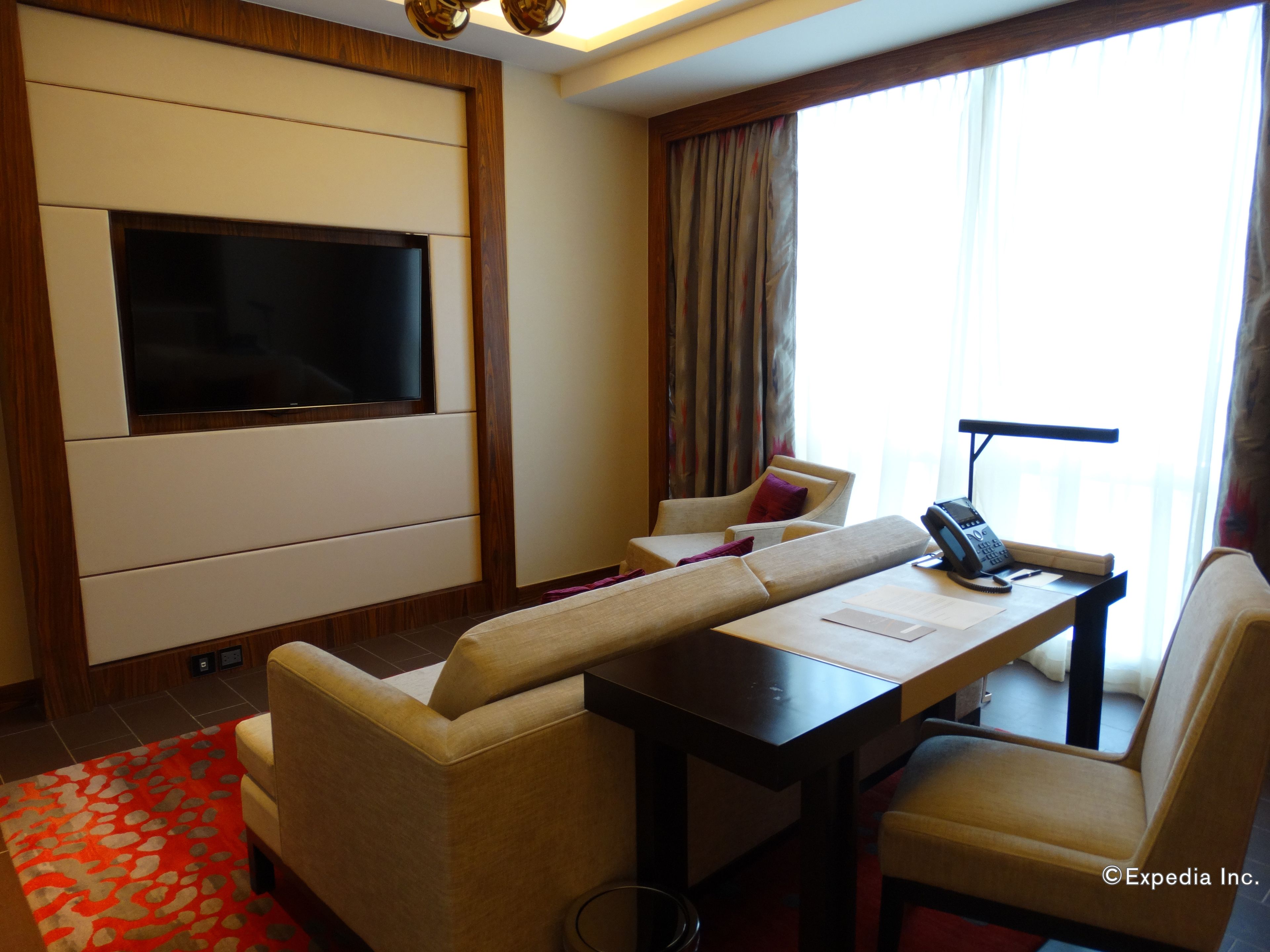 Habitación de hotel con televisión de pantalla plana en la pared, un escritorio con teléfono y dos sillones.