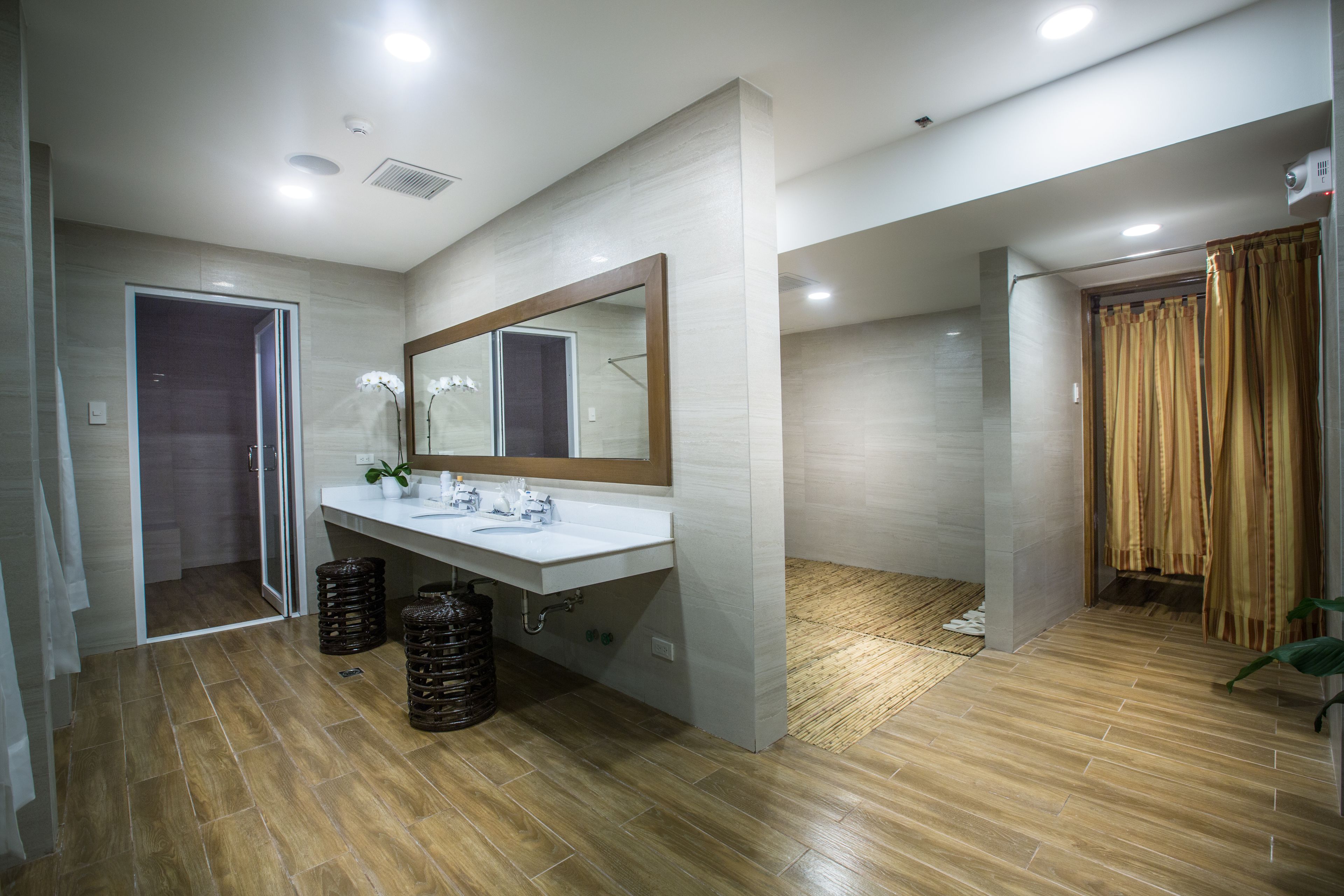 Un baño moderno con un espejo grande, lavamanos blanco y piso de madera.