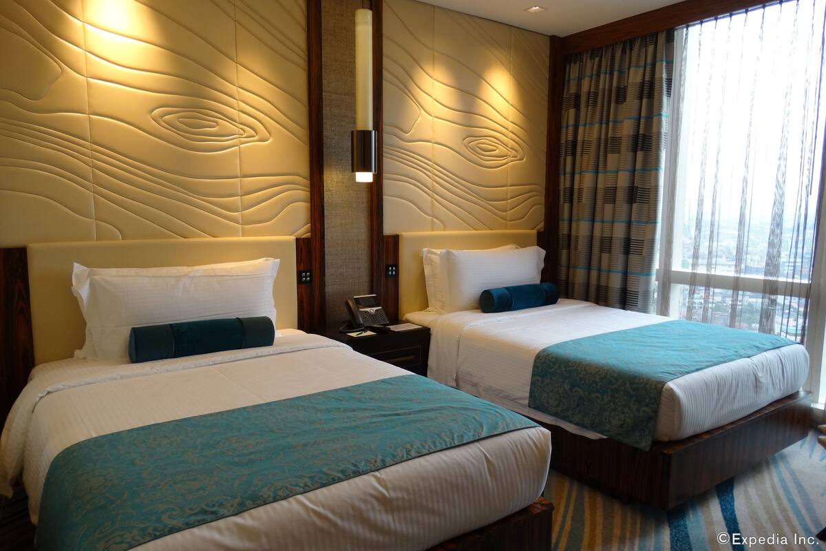 Habitación de hotel con dos camas, un espejo grande y vista a la ciudad desde la ventana.