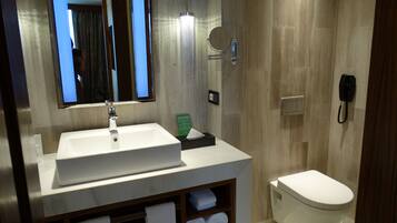 A modern bathroom with a white sink, mirror, and toilet. There is a towel rack with towels and a small shelf with toiletries.