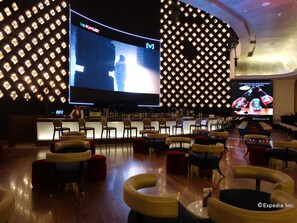Un espace bar doté d’un grand écran diffusant « The Playlist » et d’un comptoir avec diverses bouteilles. On y trouve plusieurs coins salon avec des chaises et des poufs.
