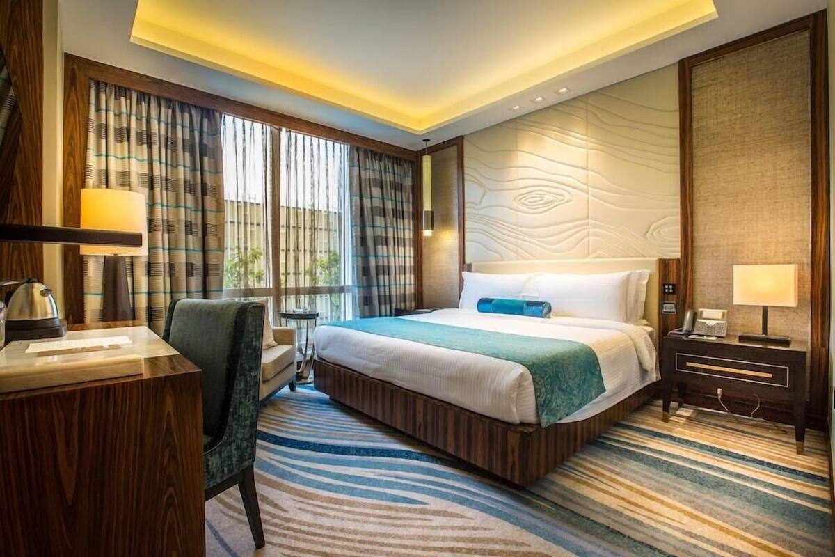 Habitación de hotel con una cama grande, un escritorio, una silla, una mesita de noche y una lámpara.
