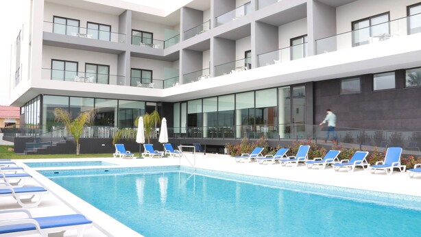 A modern hotel with a swimming pool, sun loungers, and a glass facade. - Monte Lírio Hotel (Espinho)