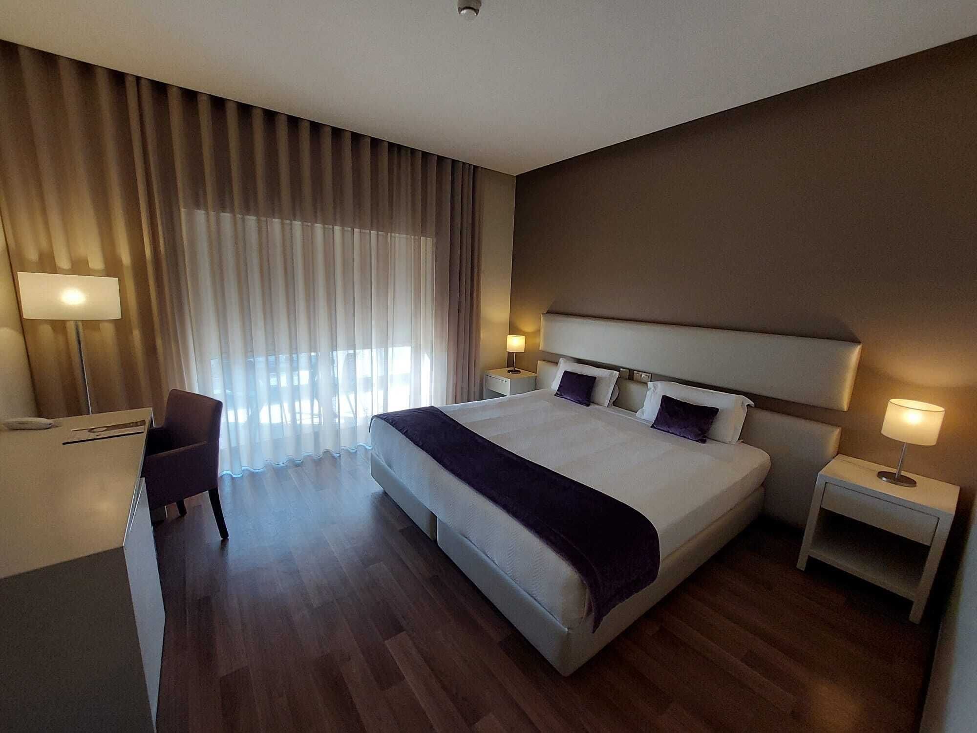 A hotel room with a large bed, two bedside tables with lamps, a desk, and a chair.