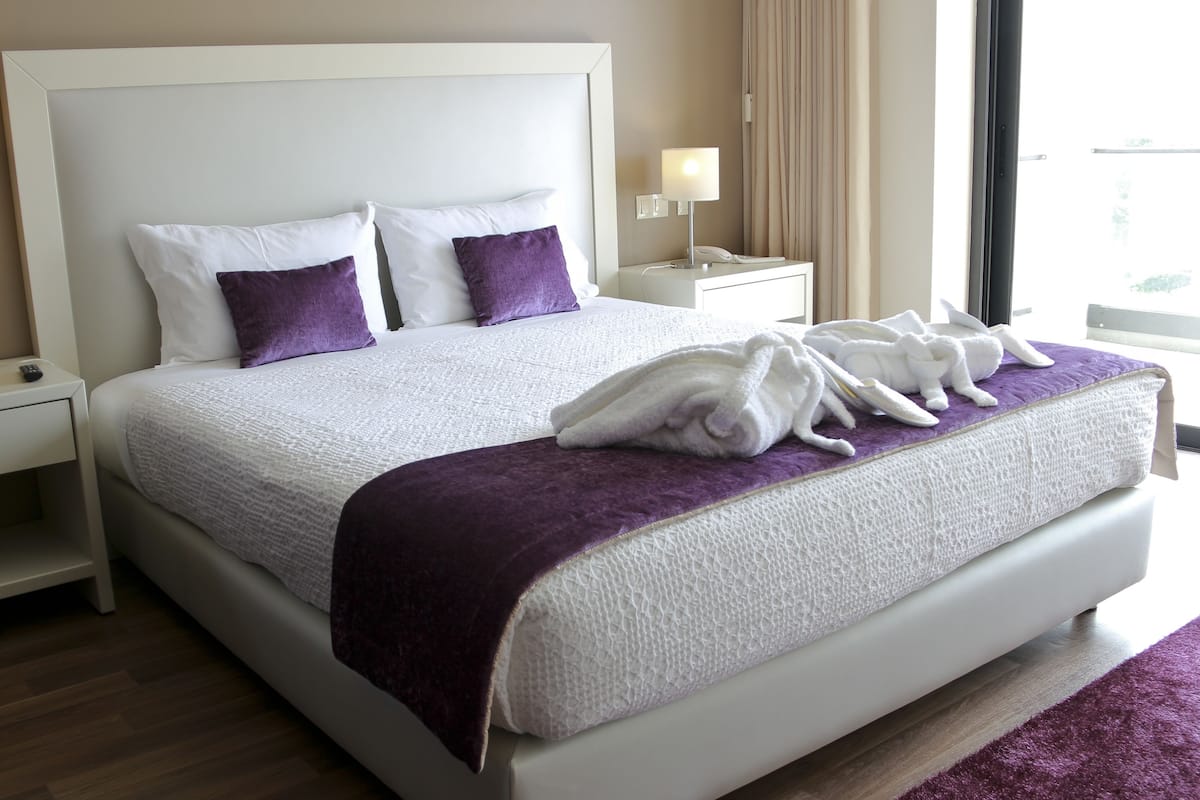 Une chambre d’hôtel avec un grand lit, deux tables de chevet, une lampe, un téléphone et une fenêtre avec des rideaux.