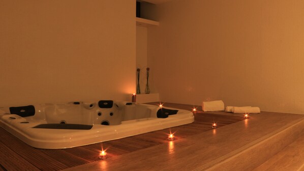 A spa room with a large bathtub, candles, and towels on the floor. - Monte Lírio Hotel (Espinho)