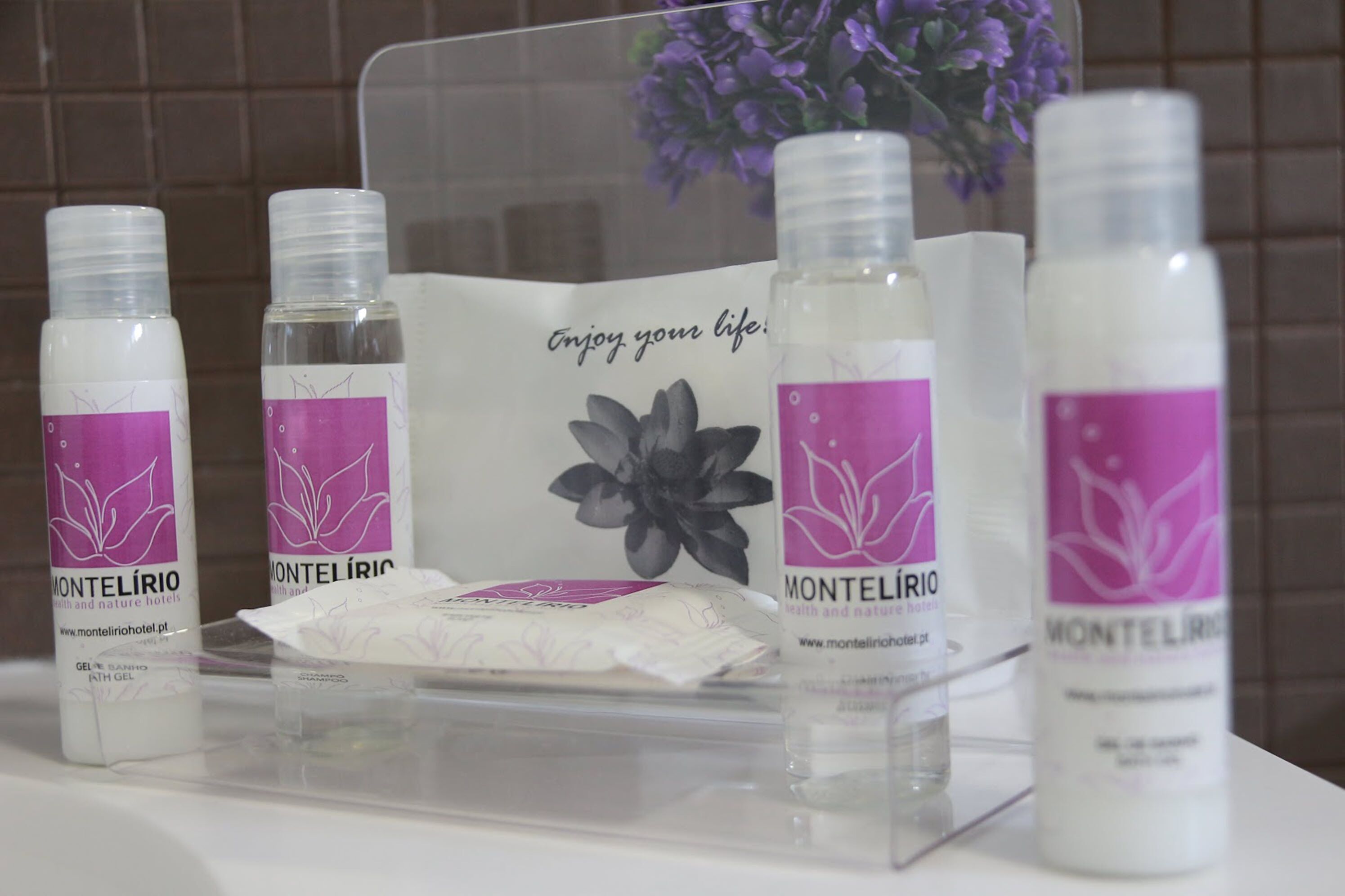 Une présentation des produits Montelírio, notamment des gels et des savons, sur un plateau transparent orné de motifs floraux, accompagnée d’une carte sur laquelle est écrit : « Profitez de la vie. »
