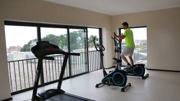 Ein Fitnessraum mit Laufband, Crosstrainer und einer Person, die den Crosstrainer benutzt.