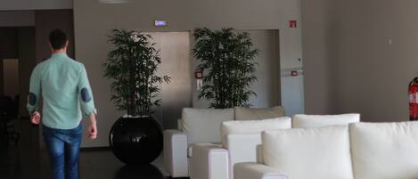 Een moderne lobby met een man in beweging, witte banken en grote kamerplanten.