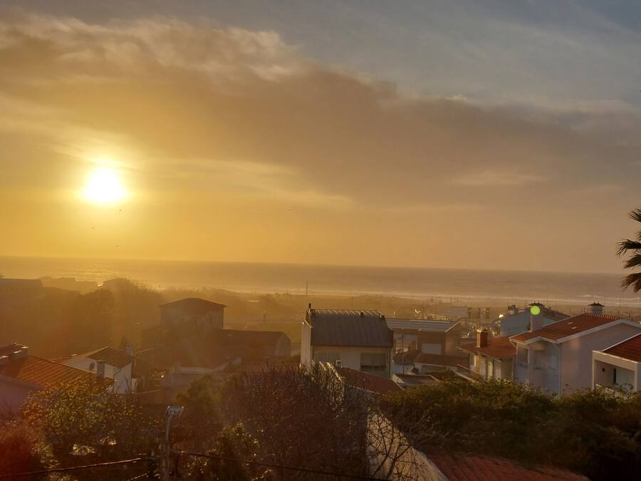Área residencial costeira com casas e vista para o mar ao pôr do sol.