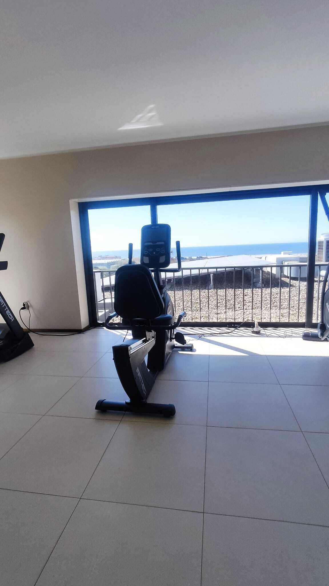 A room with a treadmill, a chair, and a view of the beach.