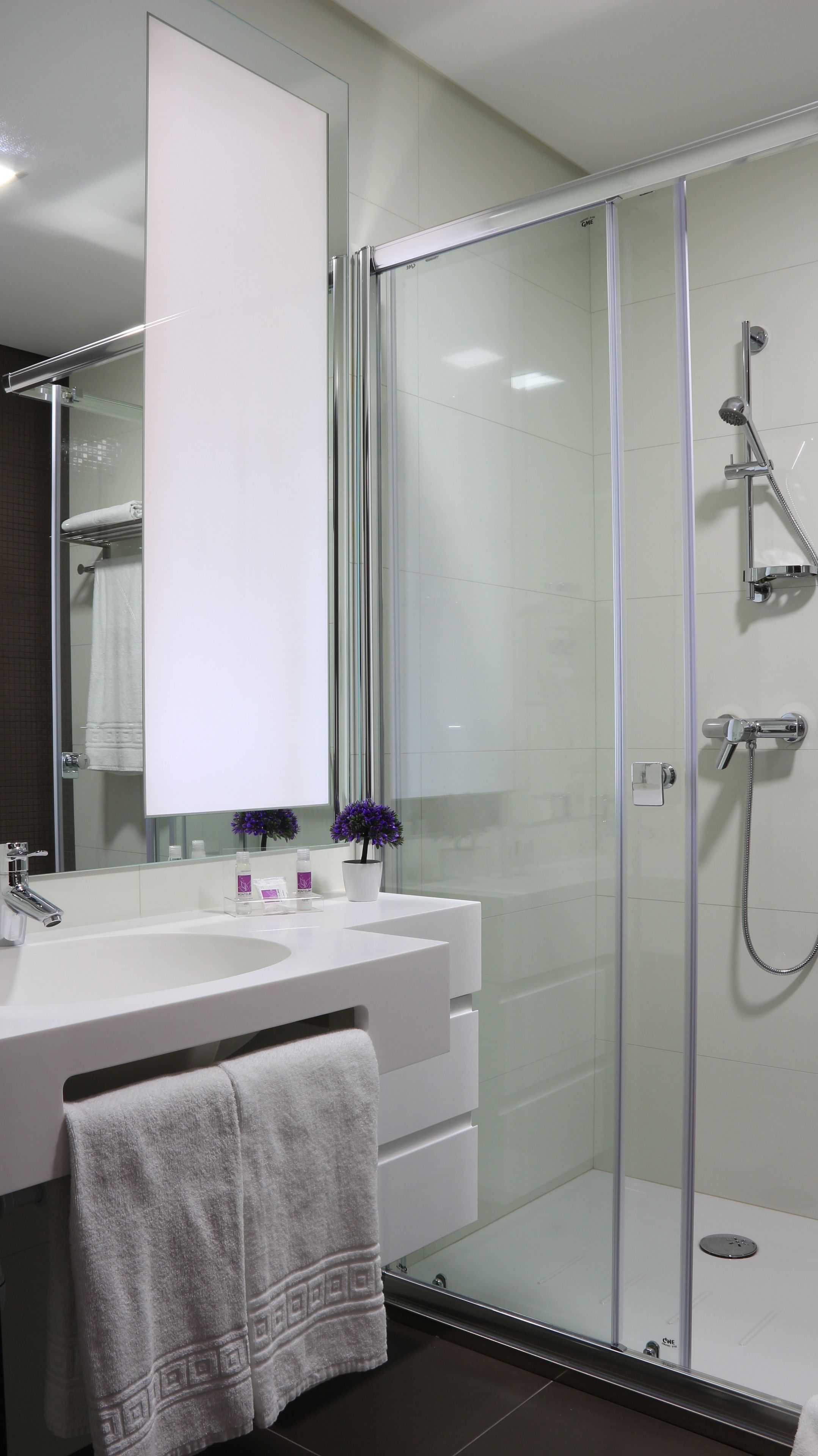 Een moderne badkamer met een douchecabine van glas, een wit wastafelmeubel met spiegel en een handdoekhouder.