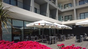 A modern outdoor seating area with white umbrellas and tables, surrounded by vibrant red flowers. - Monte Lírio Hotel (Espinho)